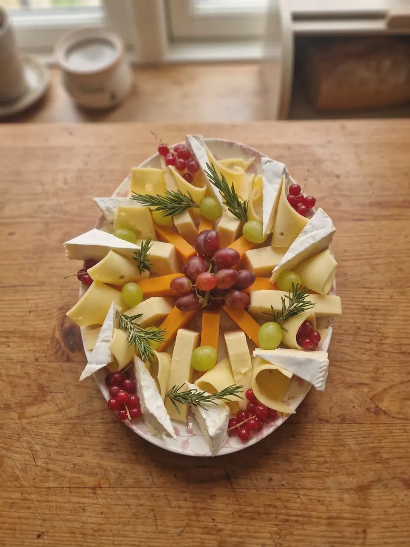 A board of cheeses with grapes, pomegranate and herbs