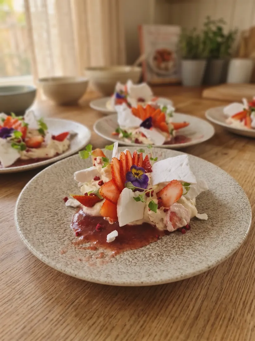 A strawberry and meringue dessert plated on speckled ceramic, with further plates behind