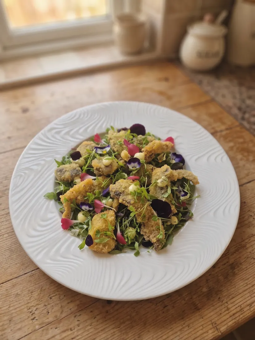 A crisp fried starter over dressed leaves and edible flowers on a white plate